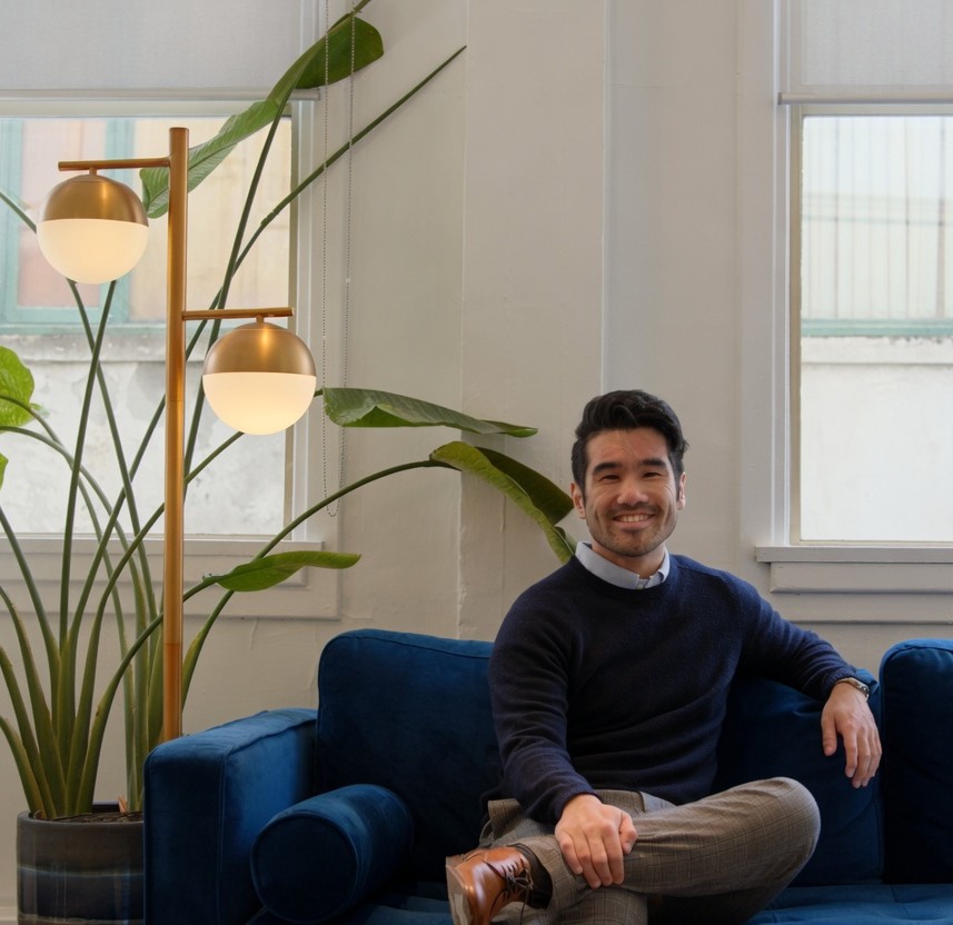 Caleb Chui, Registered Clinical Counsellor, sitting on a blue sofa in a sunlit room